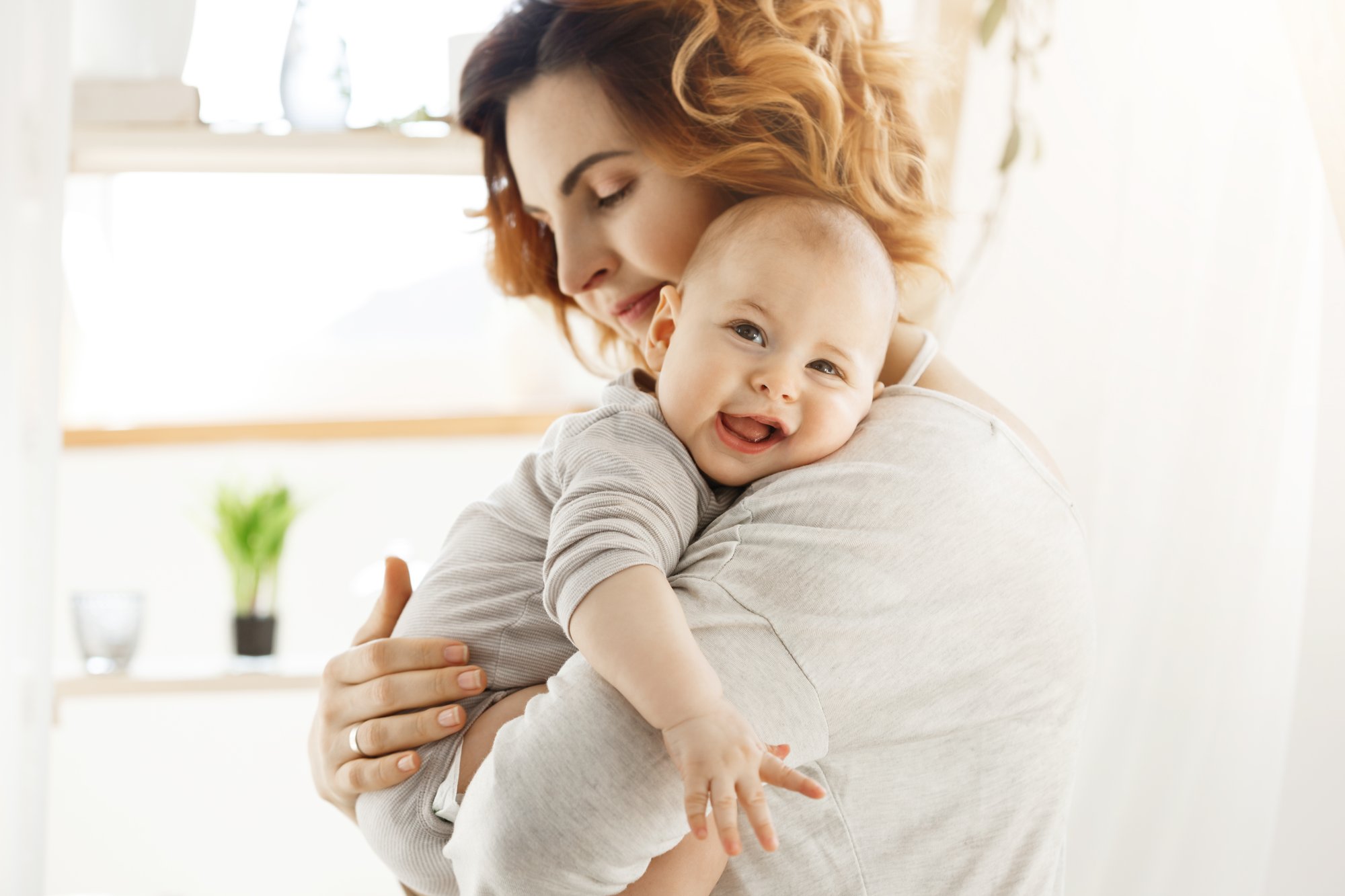 happy-young-mom-holds-precious-little-child-gently-hugging-his-little-body-kid-laughing-joyfully-looking-camera-with-big-grey-eyes